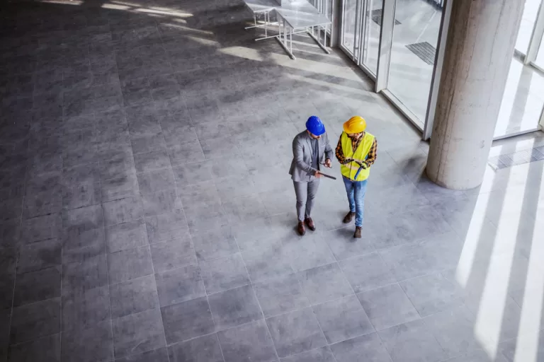 Top view of architect holding tablet and talking with construction worker about new ideas on project they working on. Building in construction process interior.