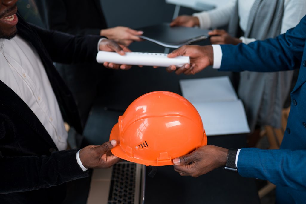 man hands over a building permit and an orange construction helmet to an investor