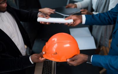 man hands over a building permit and an orange construction helmet to an investor