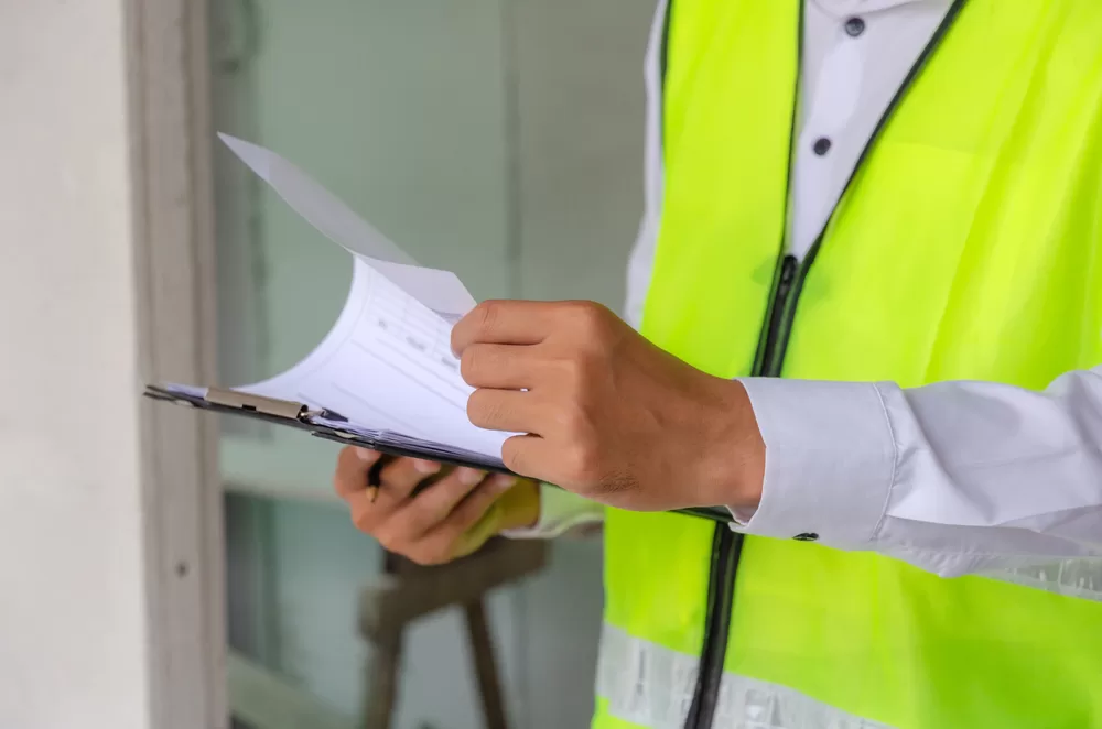 foreman builder, engineer or inspector in green safety vest reflective checking and inspecting with clipboard at construction site building interior, inspection, contractor and engineering concept